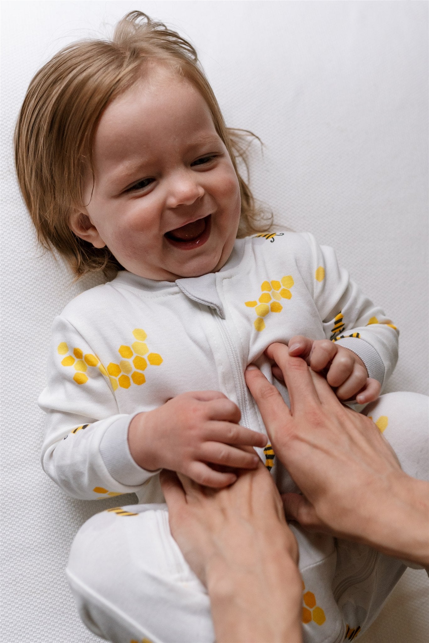 Baby wearing a white ZippyJamz sleeper with yellow bee pattern, laying on a white surface.