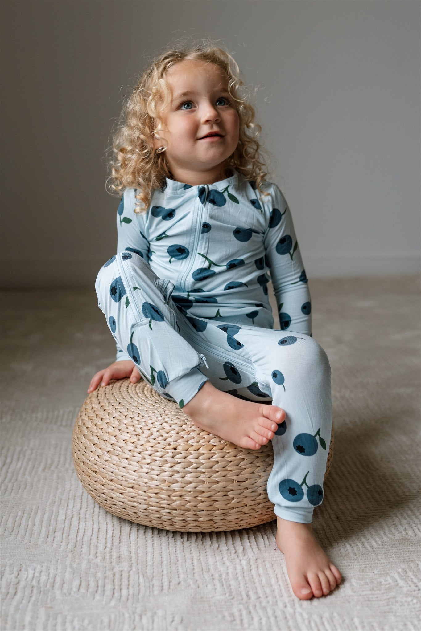 Toddler sitting on a stool wearing ZippyJamz blueberry patterned footless sleeper