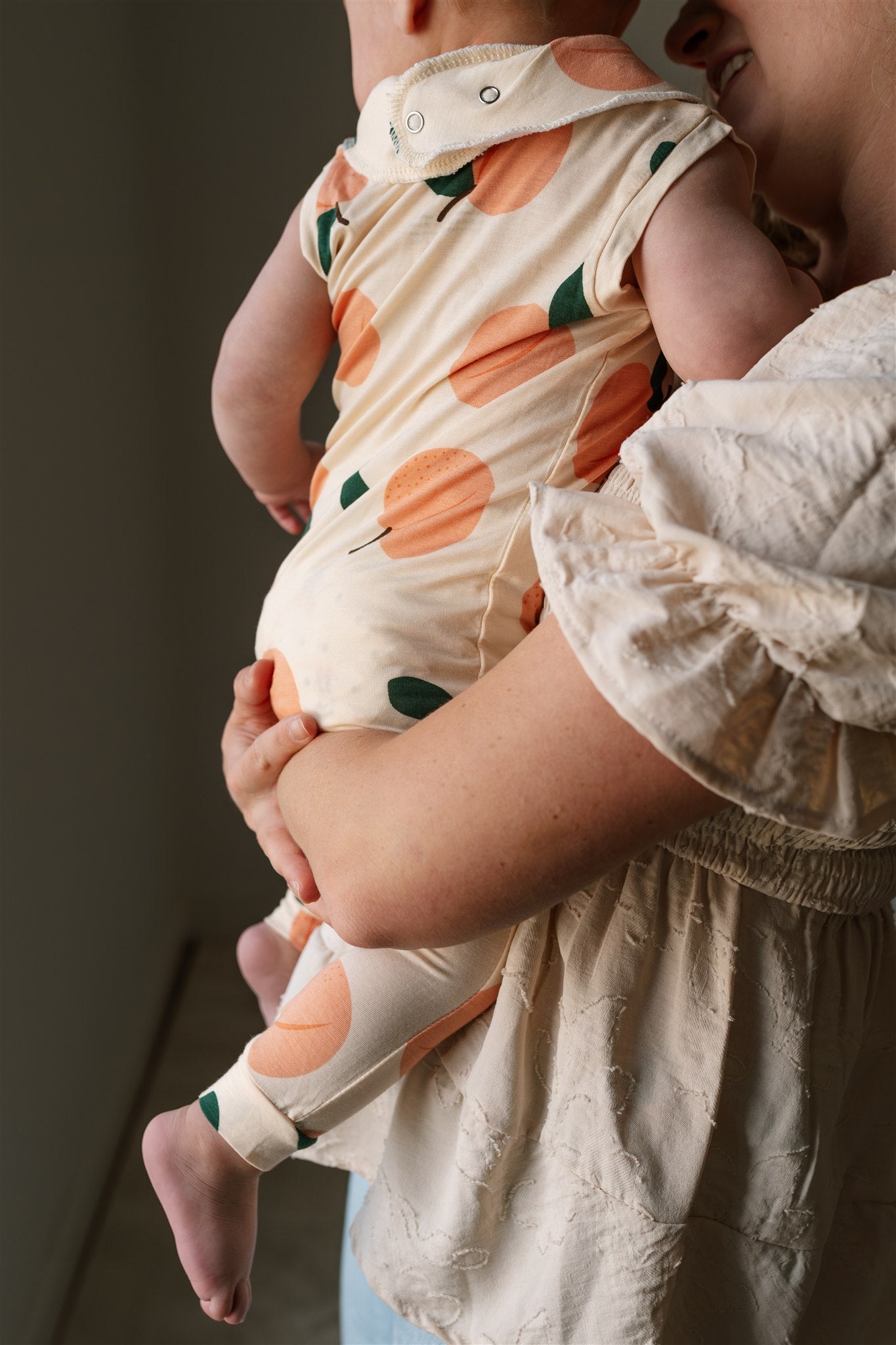 Baby wearing a ZippyJamz sleeper with peach pattern being held by an adult.