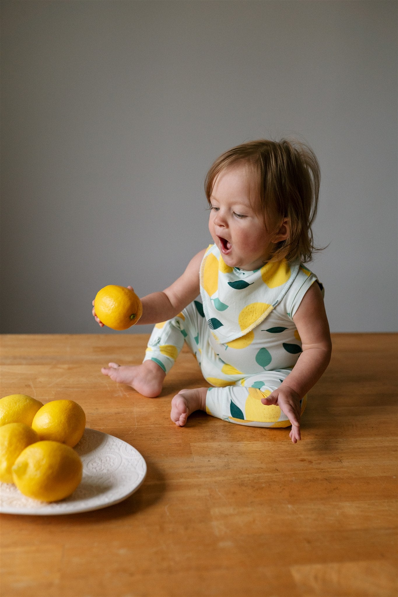 Child playing with lemons while wearing ZippyJamz lemon patterned romper