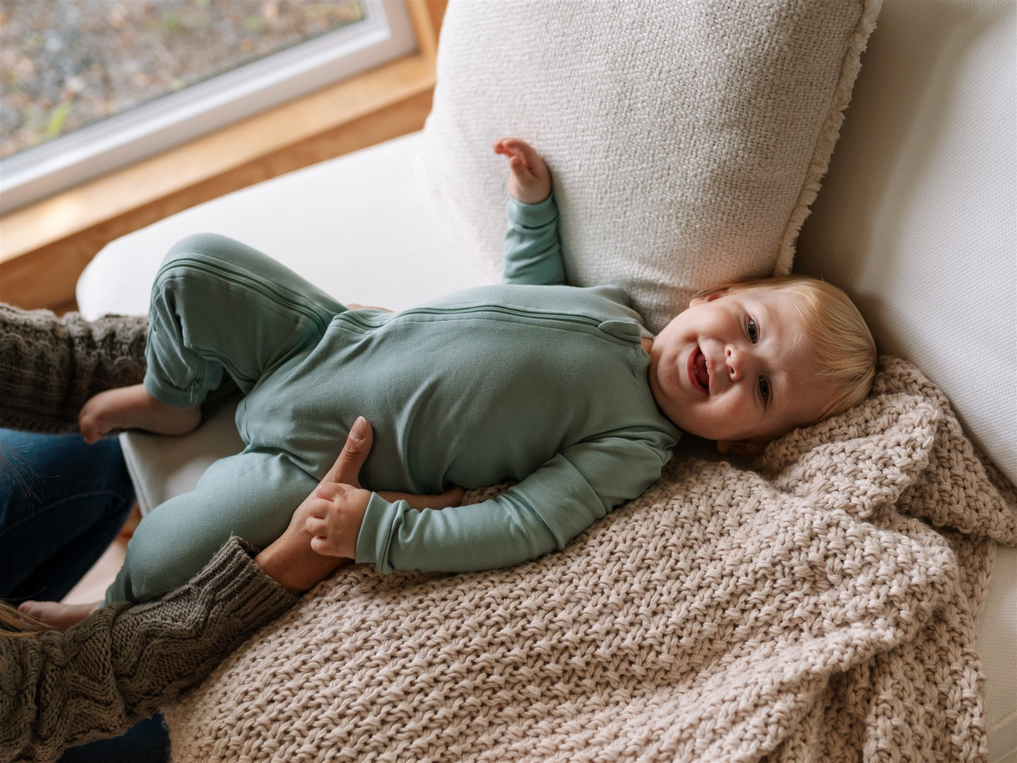 baby in green footless ZippyJamz sleeper laying on a couch with a blanket