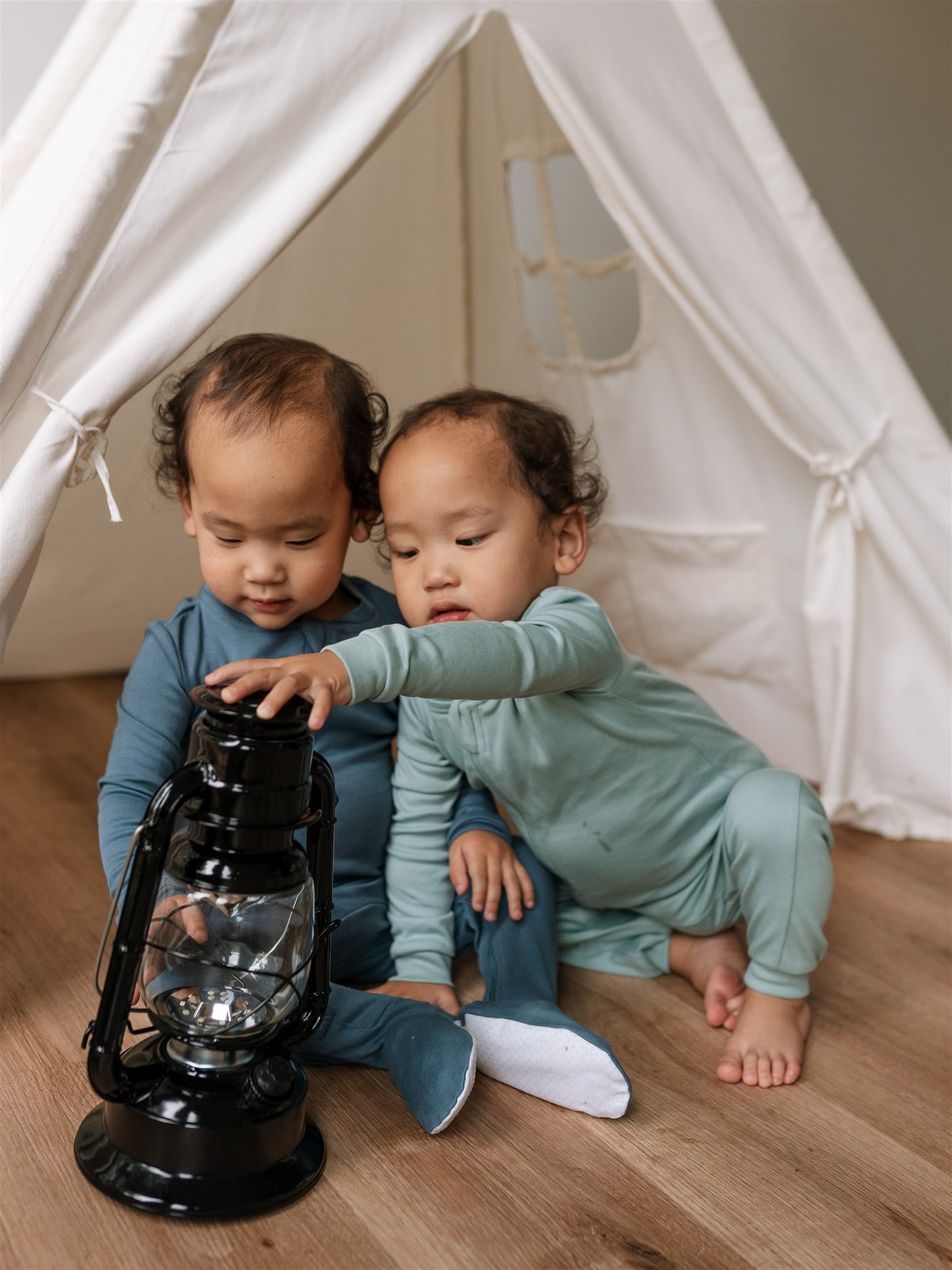 Two children playing with a black lantern while wearing Sage and Sound and True Blue ZippyJamz baby sleepers