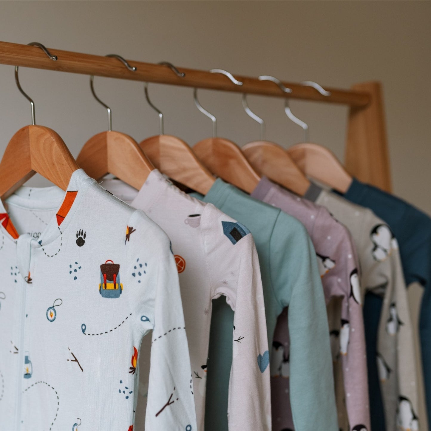 New ZippyJamz baby sleepers on wooden hangers against a neutral wall