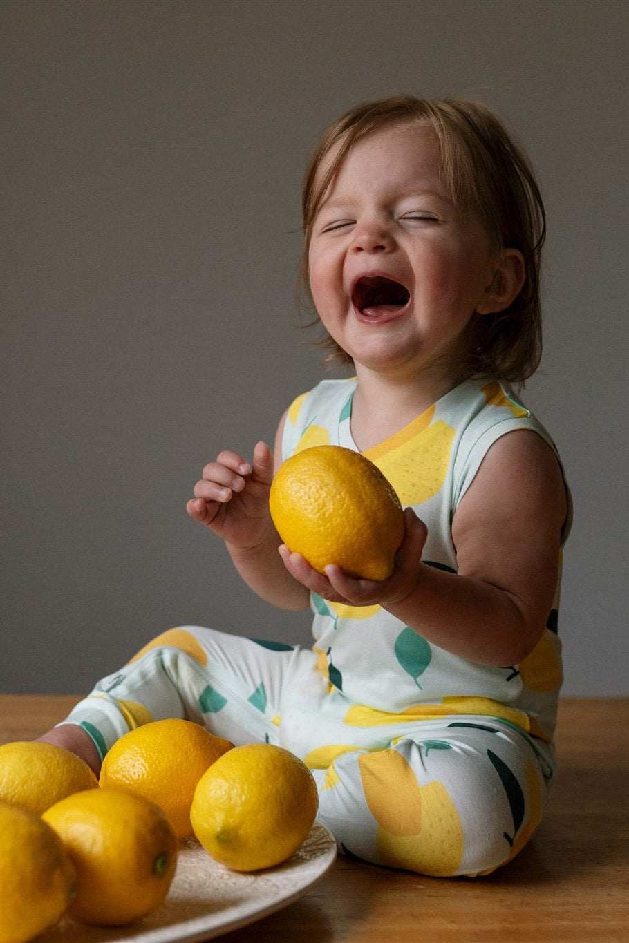 Child holding a lemon with lemons on a plate on a wooden table